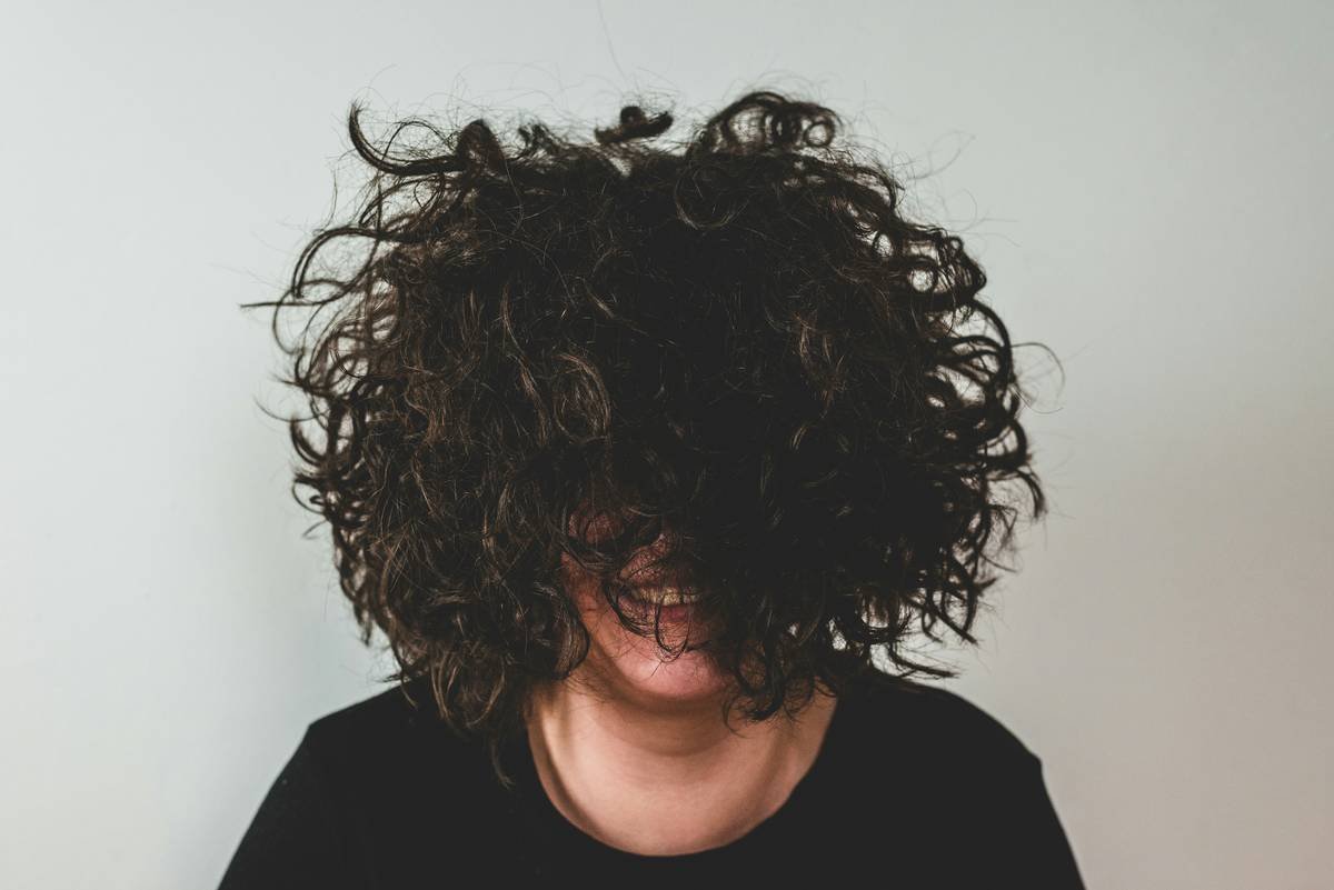 Before-and-after photos of client Maya: left shows frizzy, broken perm curls; right shows defined, shiny recovered curls after 8-week regimen