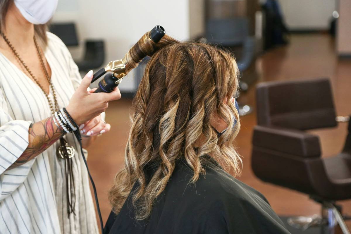 Client examining salon perm results under salon lighting showing defined curl pattern
